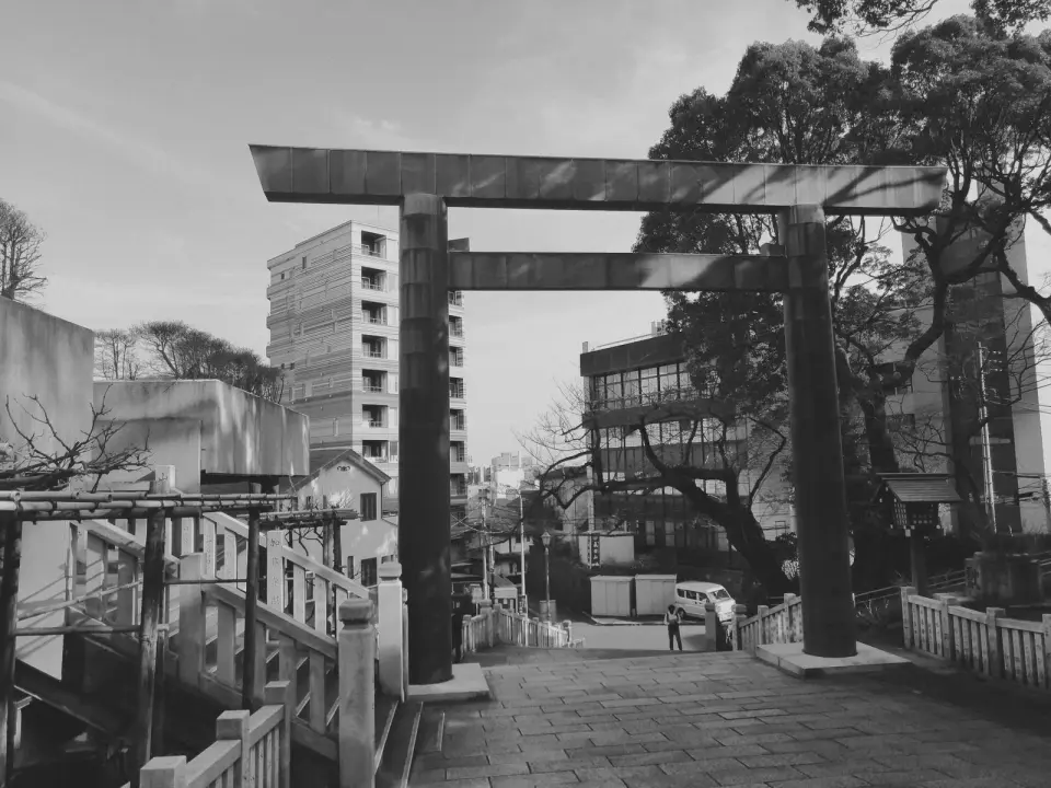 A torii gate at the top of stone steps, the town beyond. Black-and-white photo.